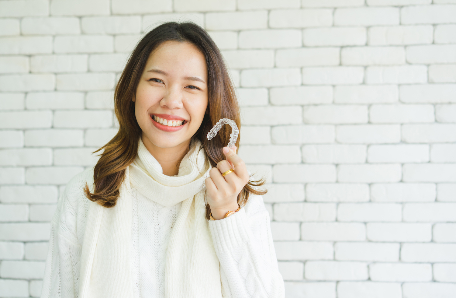 smiling woman holding up a clear aligner