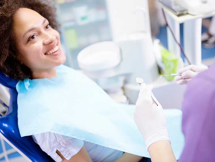 smiling woman sitting in a dental chair as her dentist prepares to examine her teeth
